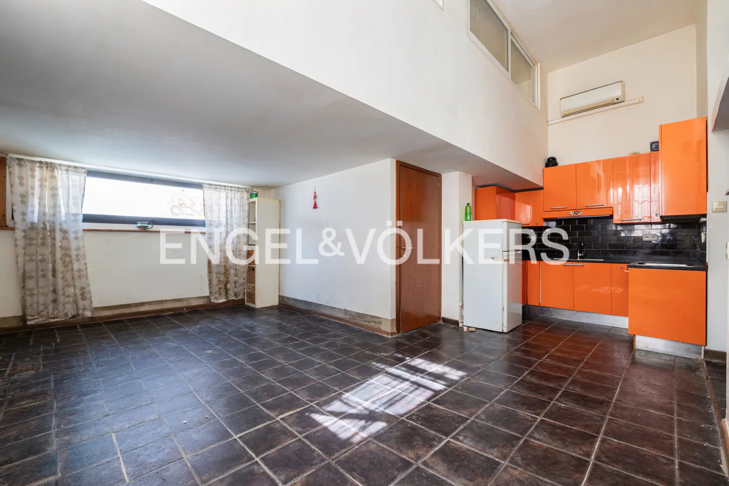 Open-concept living space with dark tile floors, orange kitchen cabinets, and a window with sheer curtains.