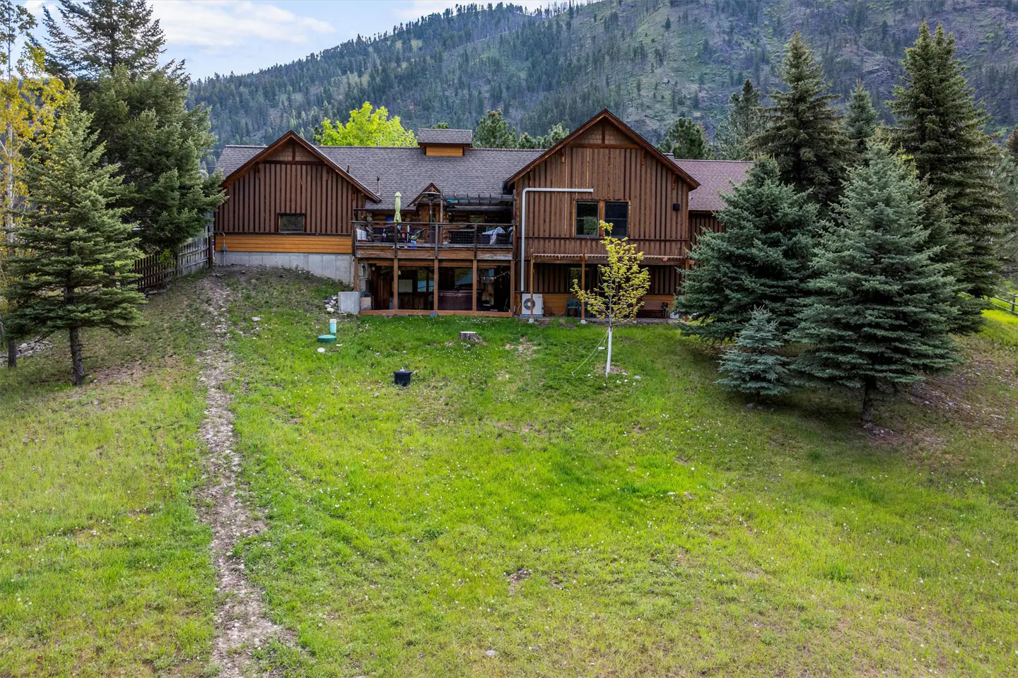 A two-story brown house with a deck and a mountain backdrop.