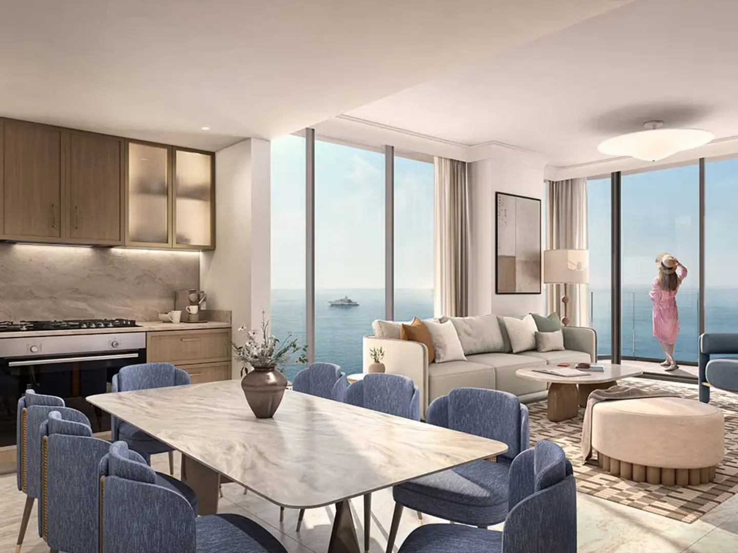 A modern apartment interior with a kitchen, dining table, and living area. A woman in a pink dress looks out at the ocean view.