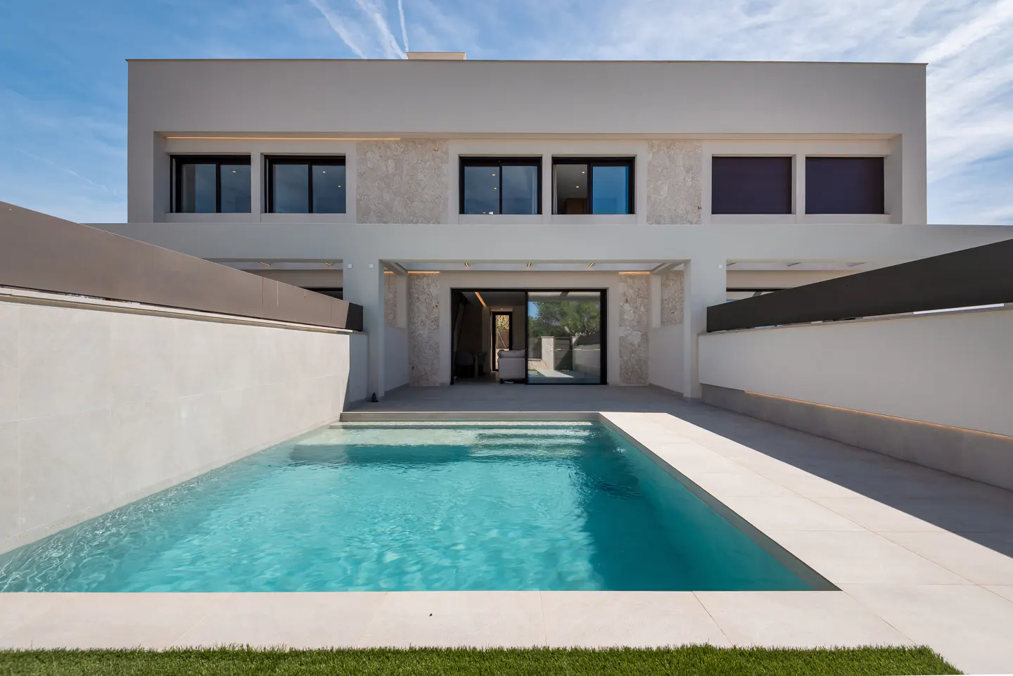Modern two-story house with a rectangular pool in the foreground. The house is white with black framed windows and a sliding glass door.
