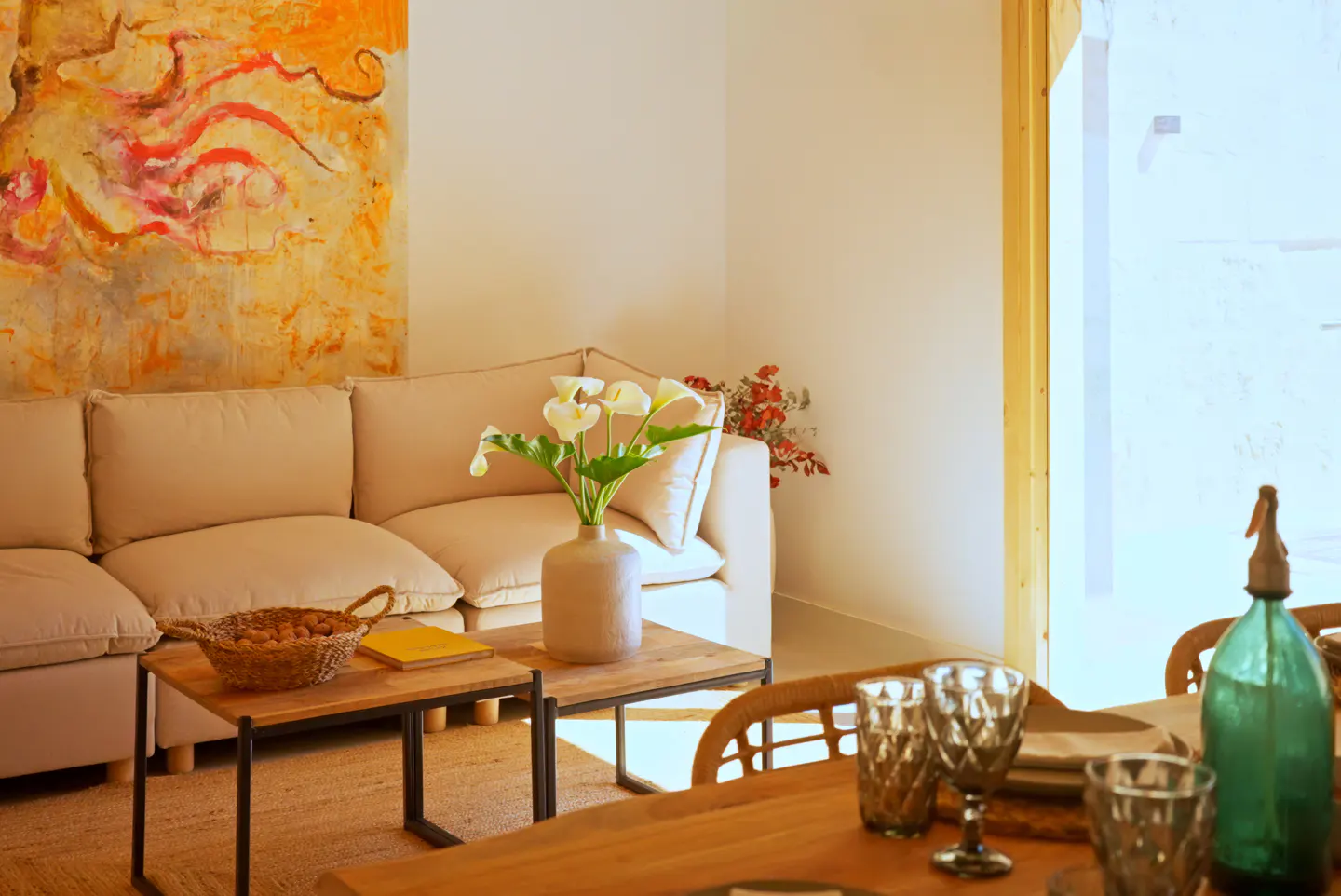 Living room with a beige sofa, abstract art, and a wooden table set with glasses and a green bottle.