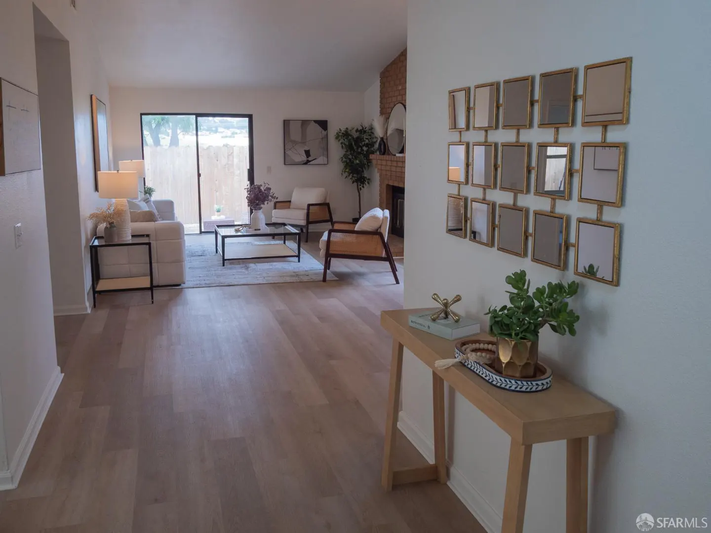 A bright living room with light wood floors, white walls, and modern furniture. A console table with decor sits near a wall with a grid of mirrors.