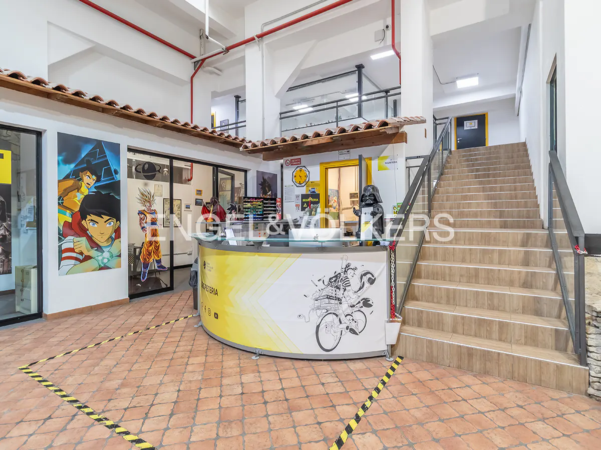 Interior view of a building lobby with a reception desk, stairs, and cartoon artwork.