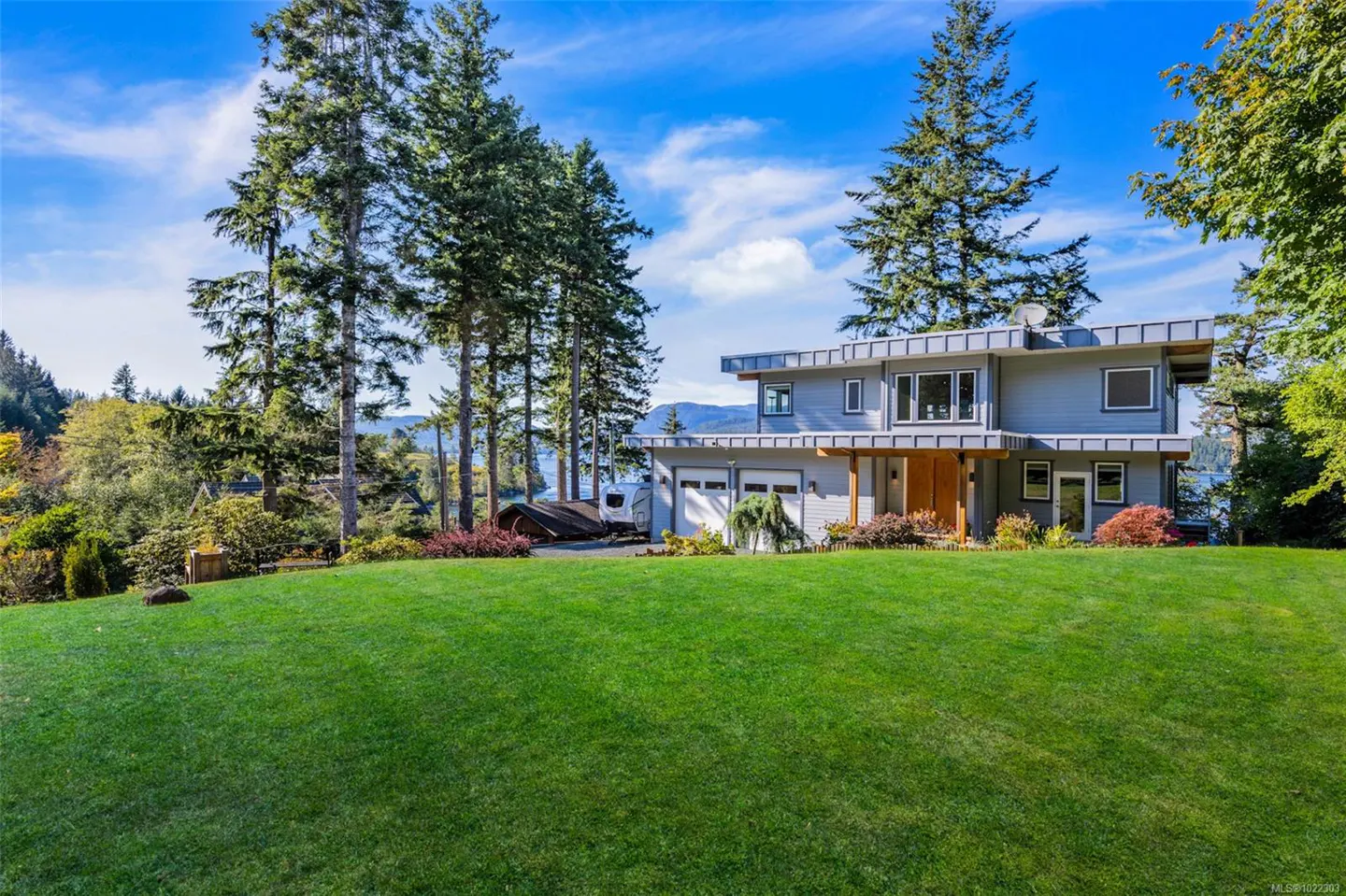 Two-story gray house with a green lawn, tall trees, and a blue sky with white clouds.