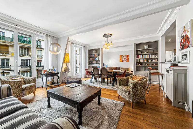 Bright living room with hardwood floors, leopard-print armchairs, a dark wood coffee table, and a dining area in the back.