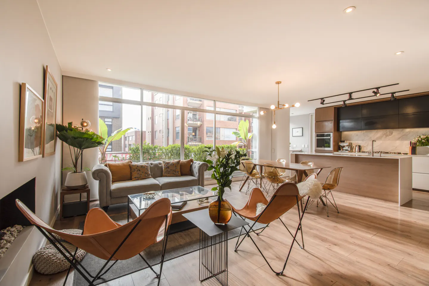 Modern open-plan living area with a grey sofa, two tan leather butterfly chairs, dining table, and sleek kitchen.