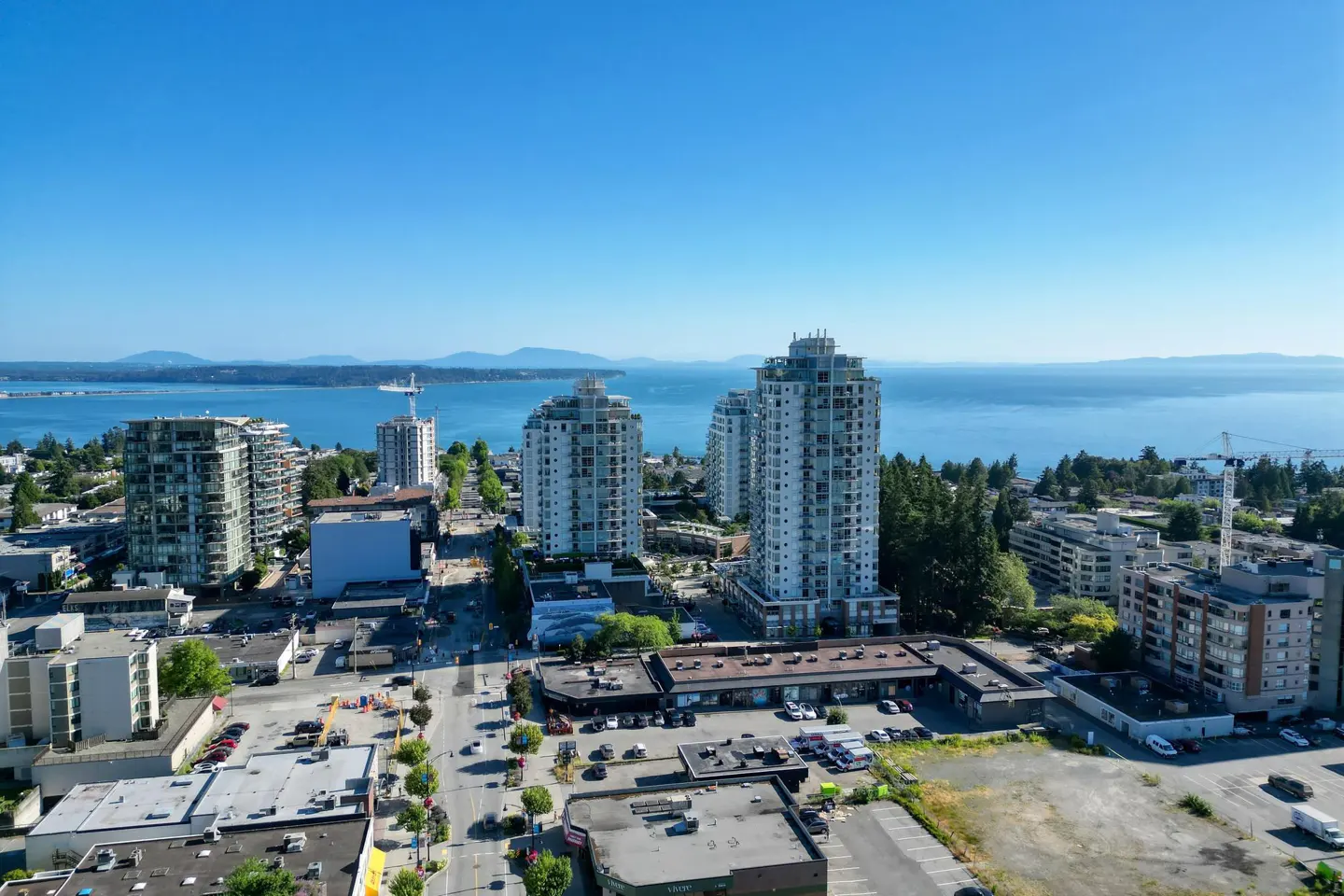 Aerial view of a city with tall buildings, streets, and a blue ocean in the background under a clear blue sky.