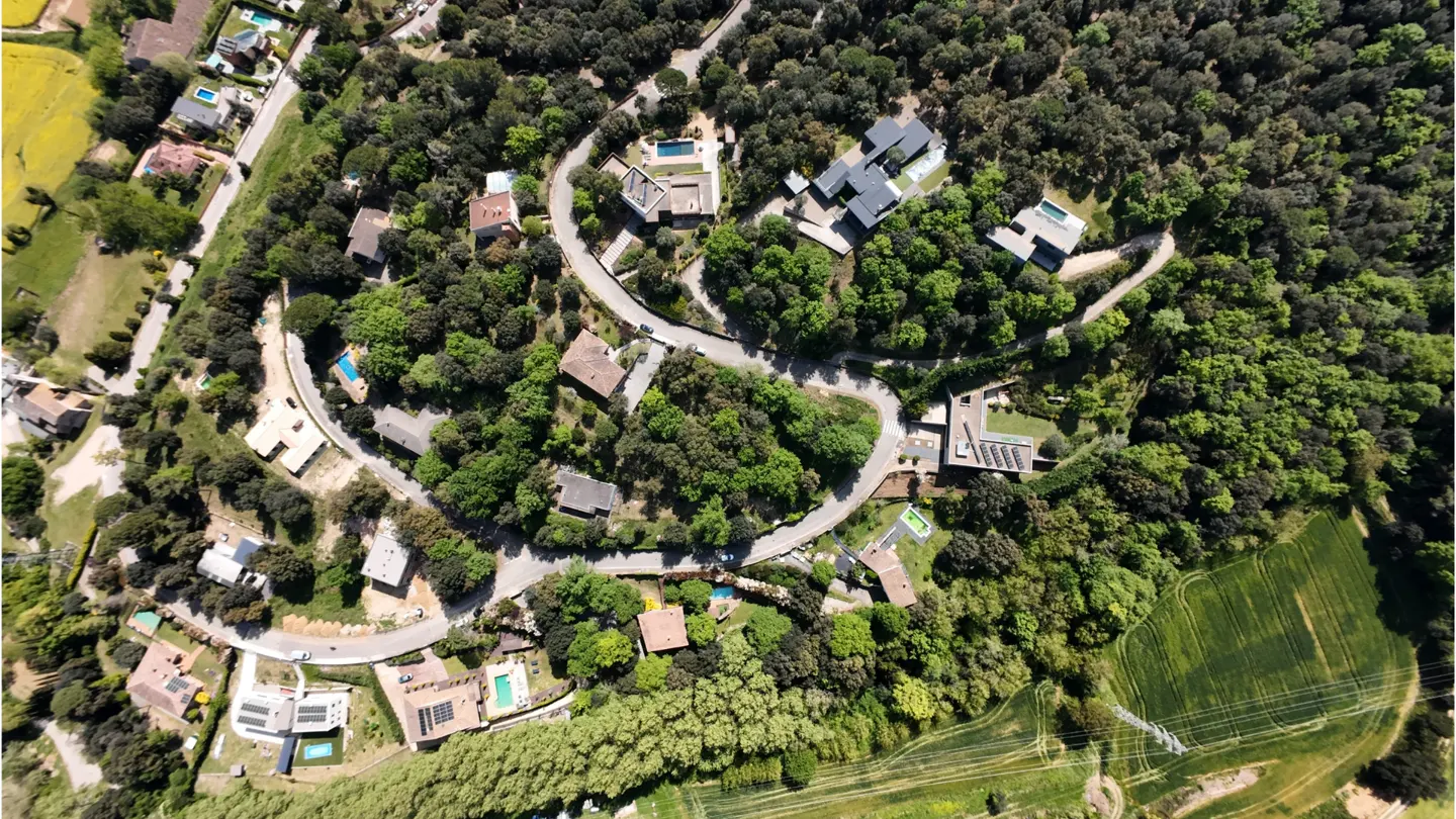 Aerial view of luxury homes nestled in green trees along a winding road. Some homes have pools.