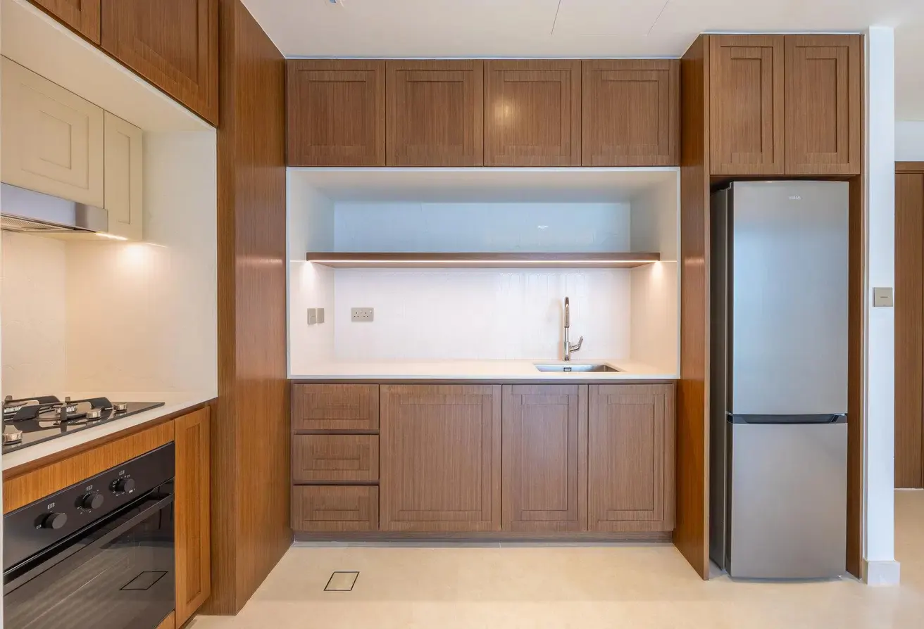 A modern kitchen with brown cabinets, a stainless steel refrigerator, and a white countertop with a sink.