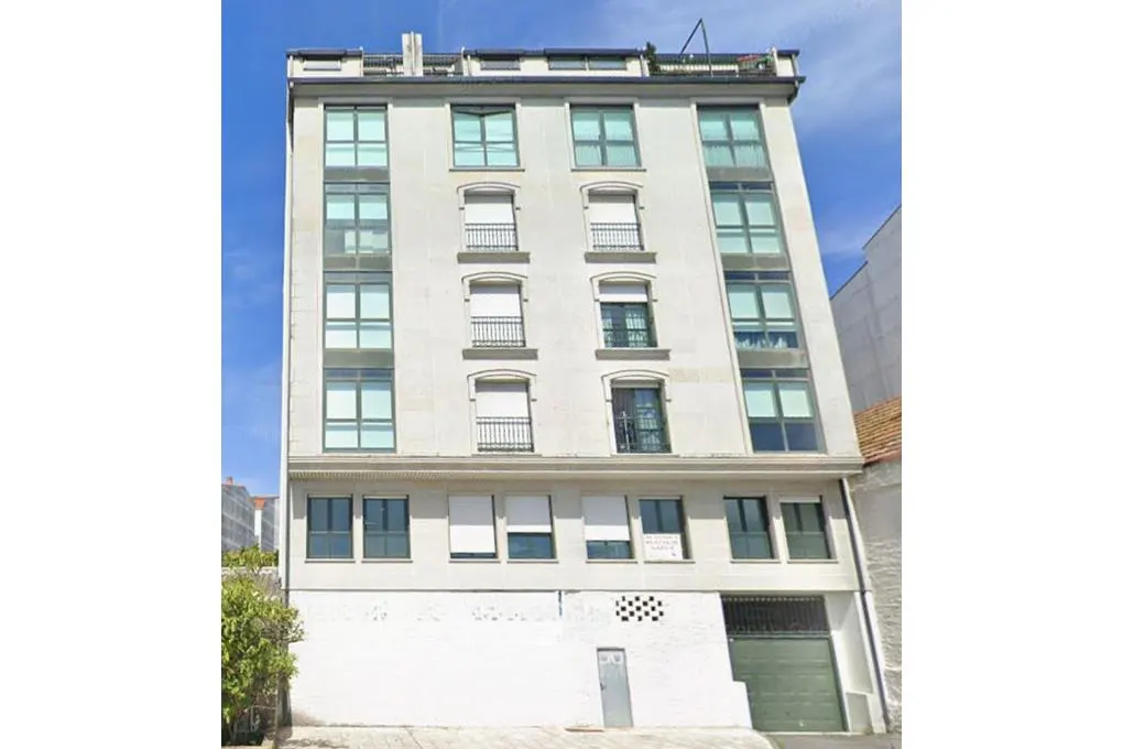 A tall, light-colored apartment building with multiple windows, small balconies, and a ground-level garage door.