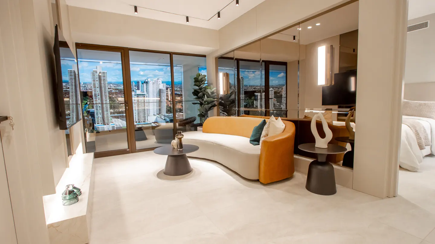 Modern apartment living room with a curved sofa, city view through glass doors, and a glimpse of the bedroom.