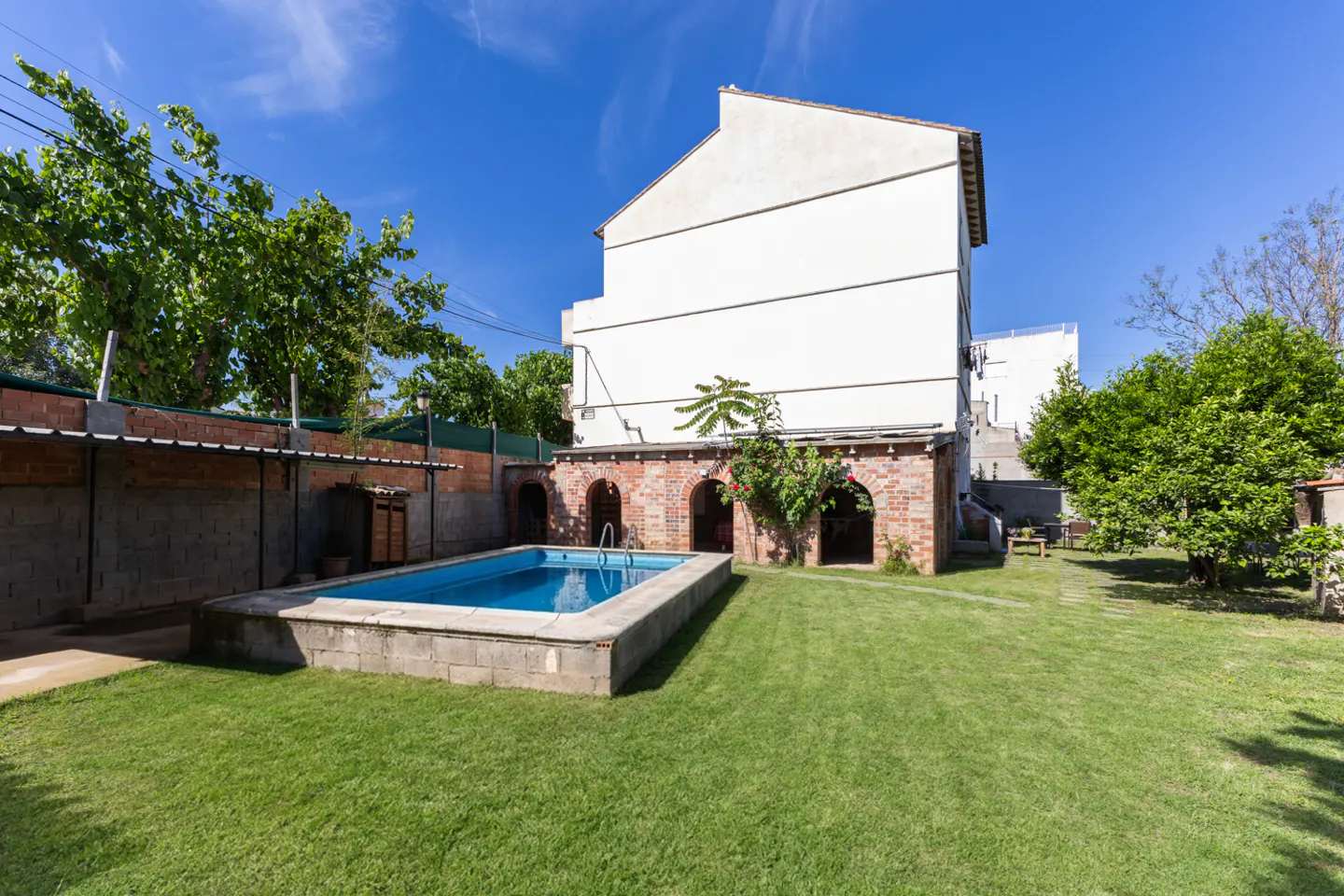 Backyard view of a white building with a blue swimming pool, green grass, and brick arches.