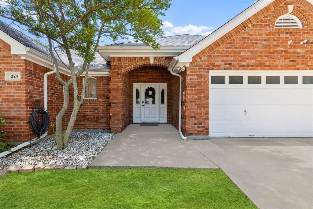 Red brick house with white trim, a white garage door, and a white front door with a wreath. A tree is on the left.