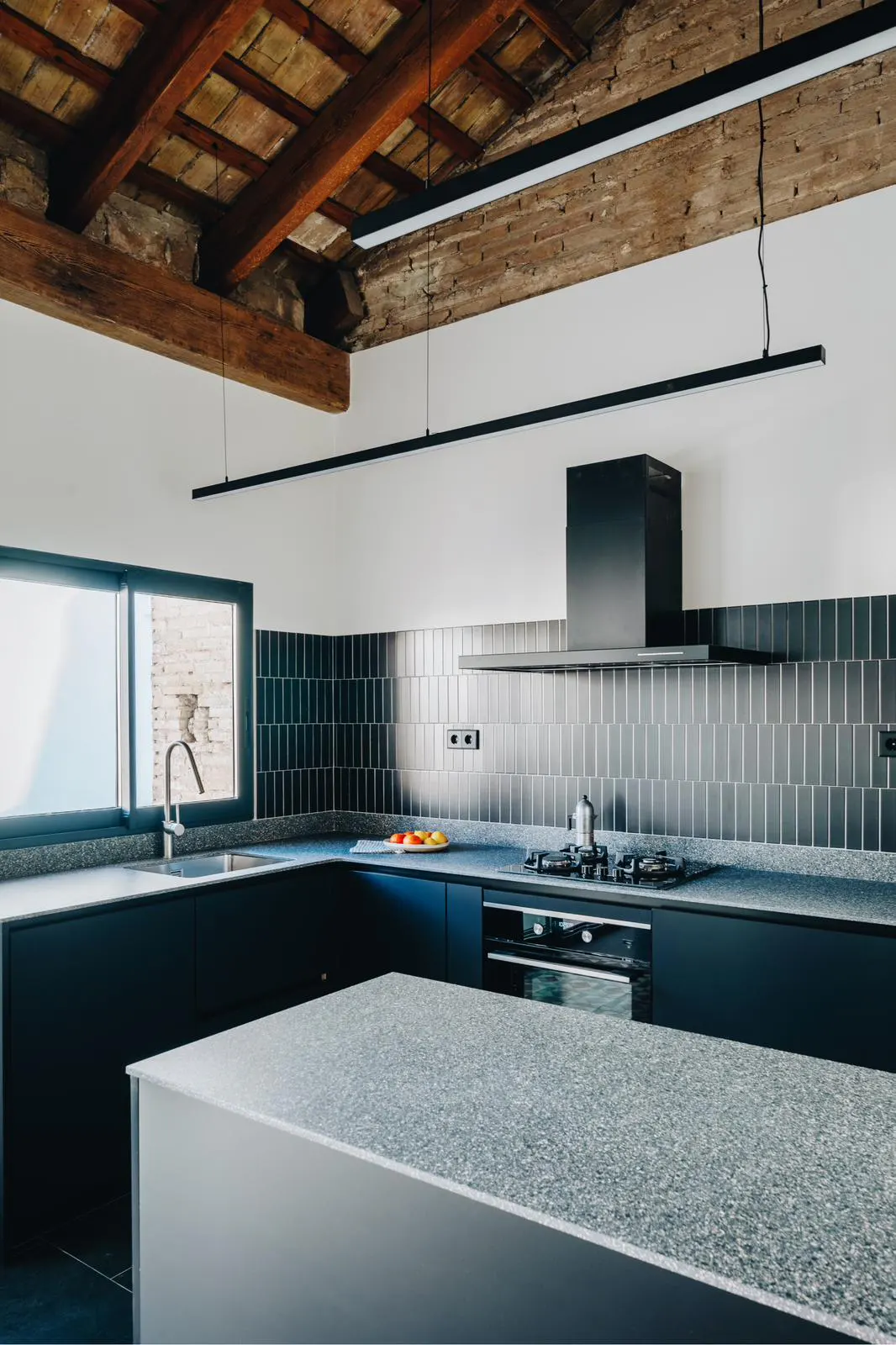 Modern kitchen with dark blue cabinets, gray countertops, and a black range hood. The ceiling has exposed wooden beams.