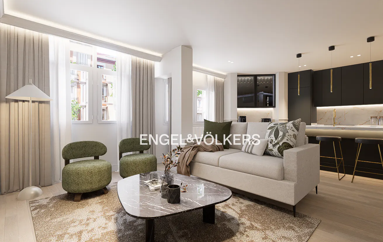 Modern living room with a beige sofa, two green armchairs, a marble coffee table, and an open kitchen with black cabinets.