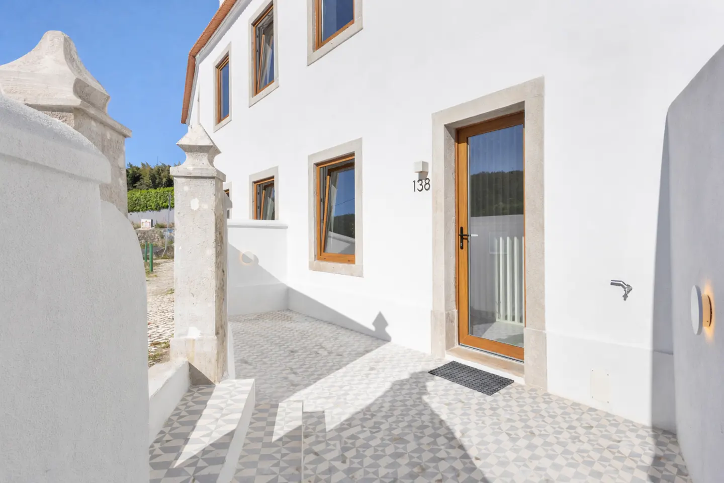 Exterior view of a white two-story house with brown window frames and a wooden door with the number 138 above it.