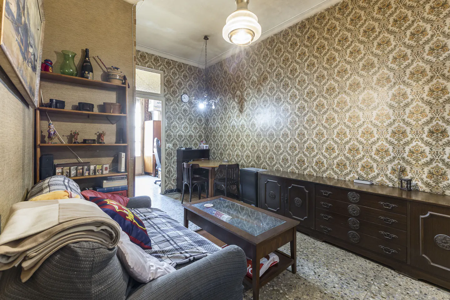 A living room with patterned wallpaper, a gray sofa, a wooden coffee table, and a long dark wood dresser.