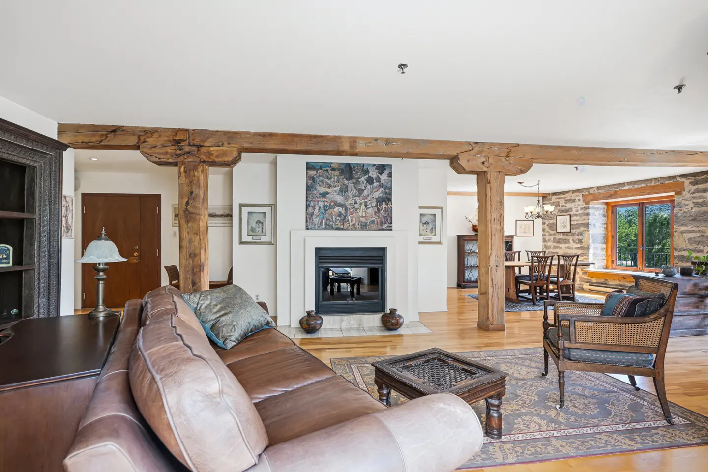 Living room with a brown leather sofa, wooden beams, fireplace, and dining area in the background.