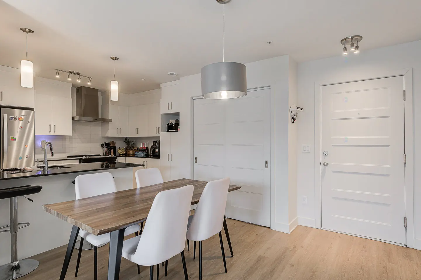 A bright, modern apartment interior with a kitchen, dining table, and white front door.