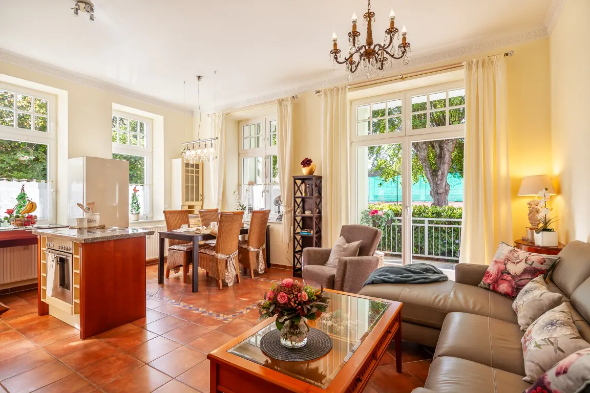 Bright, open-plan living space with terracotta tile flooring, a dining table, a leather sofa, and large windows overlooking a garden.