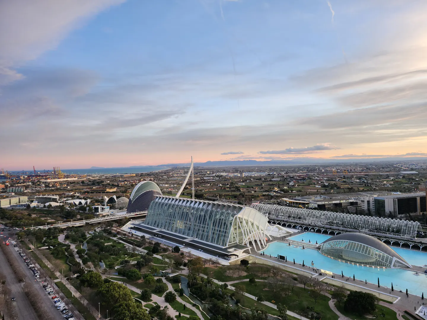 Aerial view of Valencia's City of Arts and Sciences, featuring modern architecture, blue pools, and green spaces under a pastel sky.