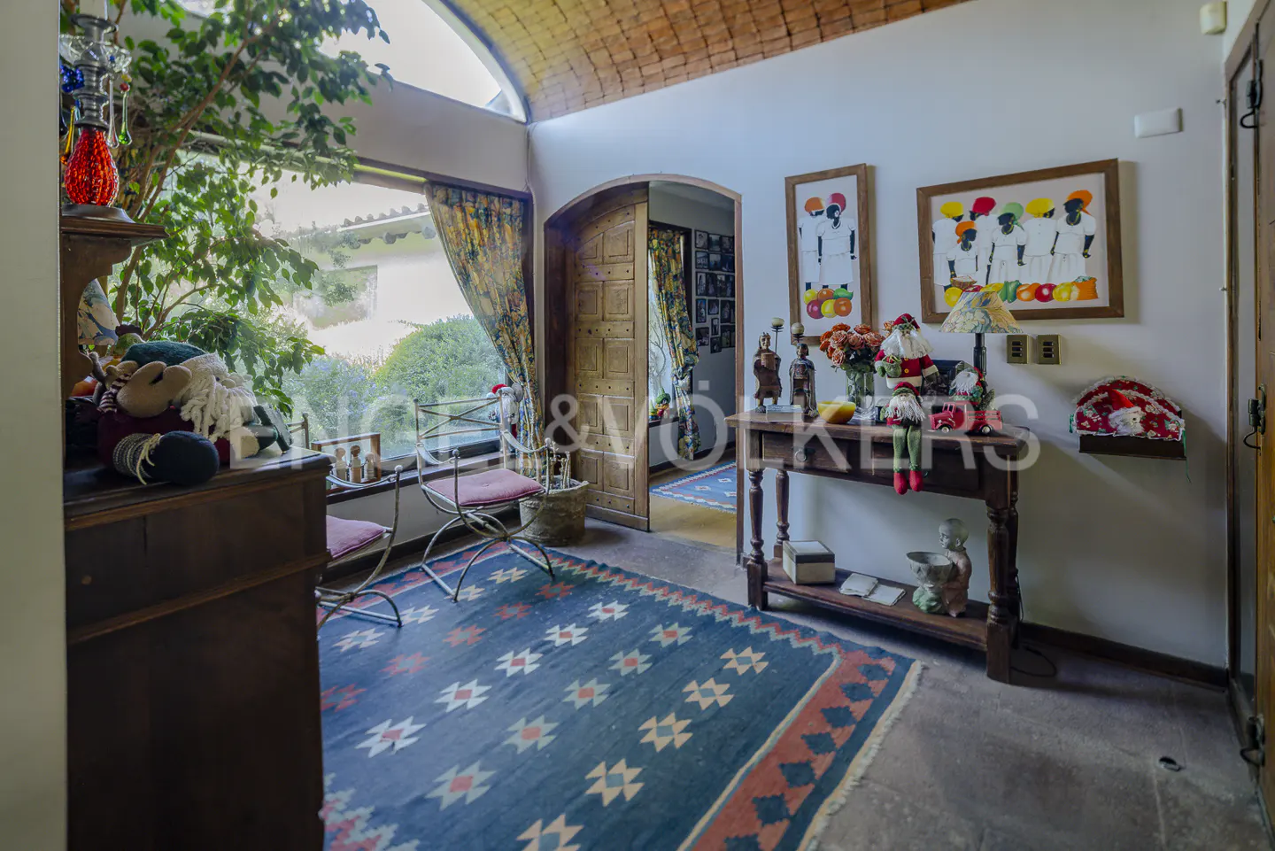 Cozy entryway with a patterned blue rug, wooden console table, Christmas decor, and a large window with garden views.