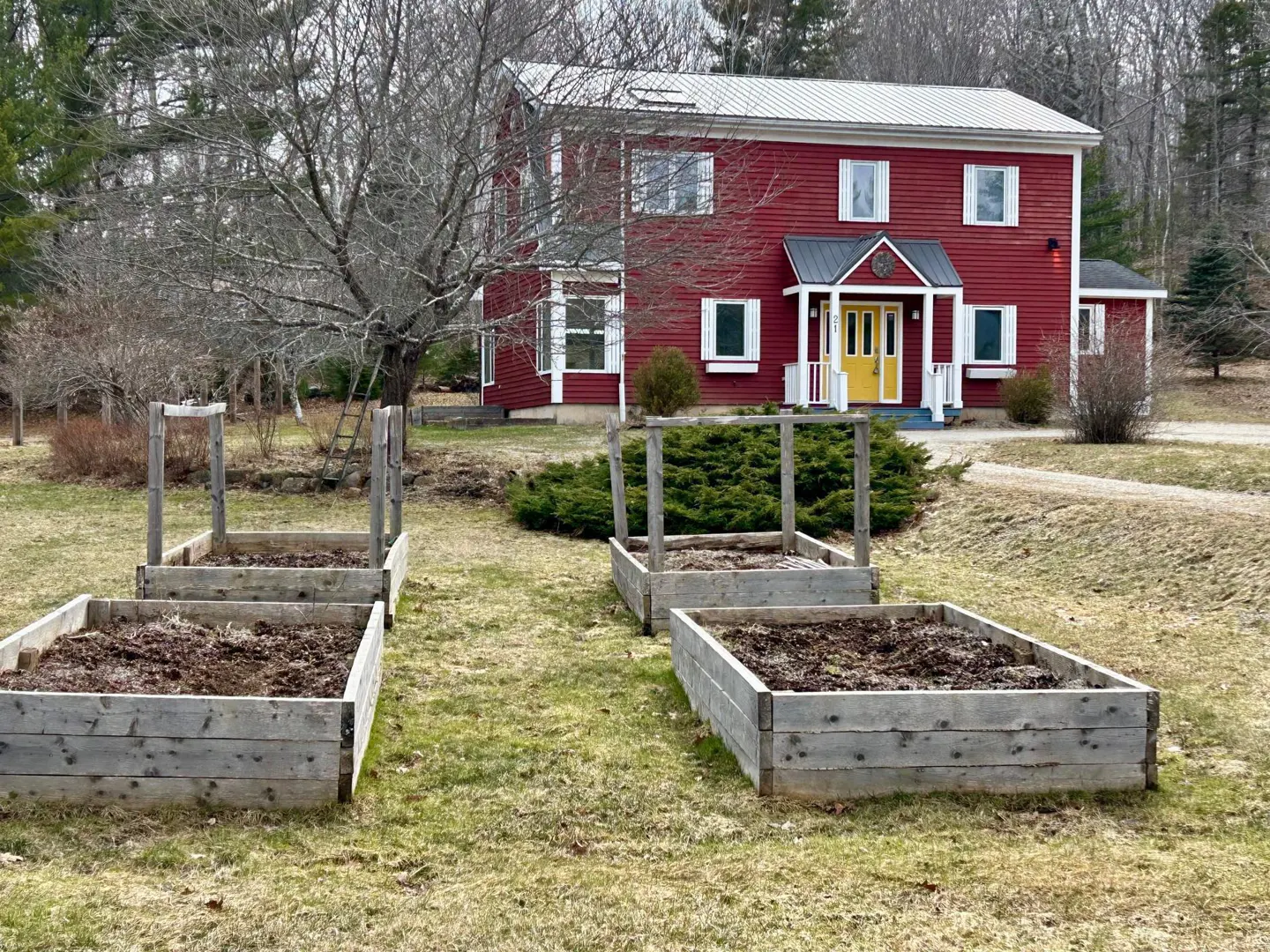 A red two-story house with a yellow door and white trim, and three raised garden beds in the front yard.