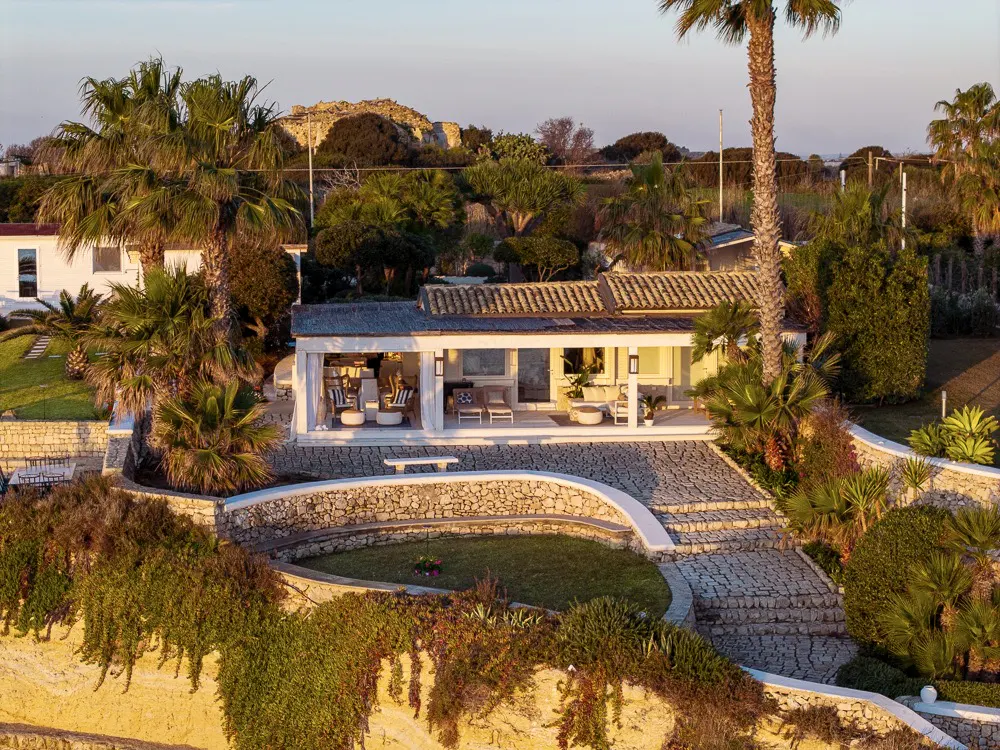 Exterior view of a white, modern beach house with palm trees and stone steps leading to the entrance.