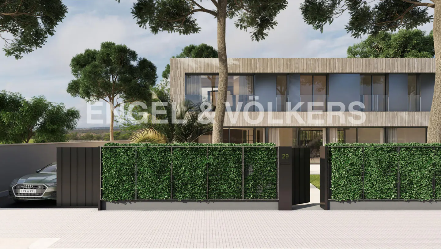 Modern two-story house with wood siding, large windows, and a green hedge fence. A gray car is parked behind a black gate.