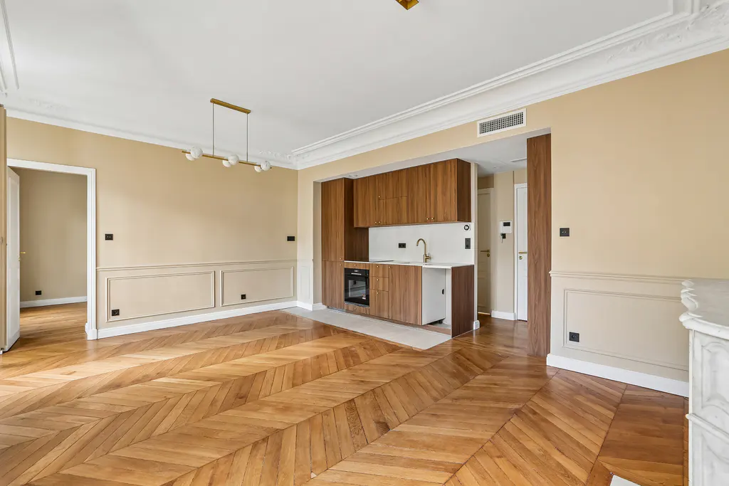 Modern kitchen with wood cabinets, herringbone parquet floors, and beige walls in a bright, open-plan living space.