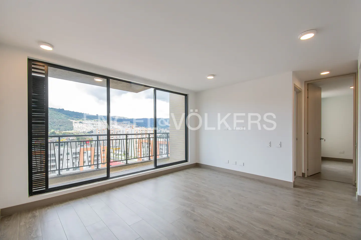 Bright, empty room with wood floors, white walls, and a large window with a city view.
