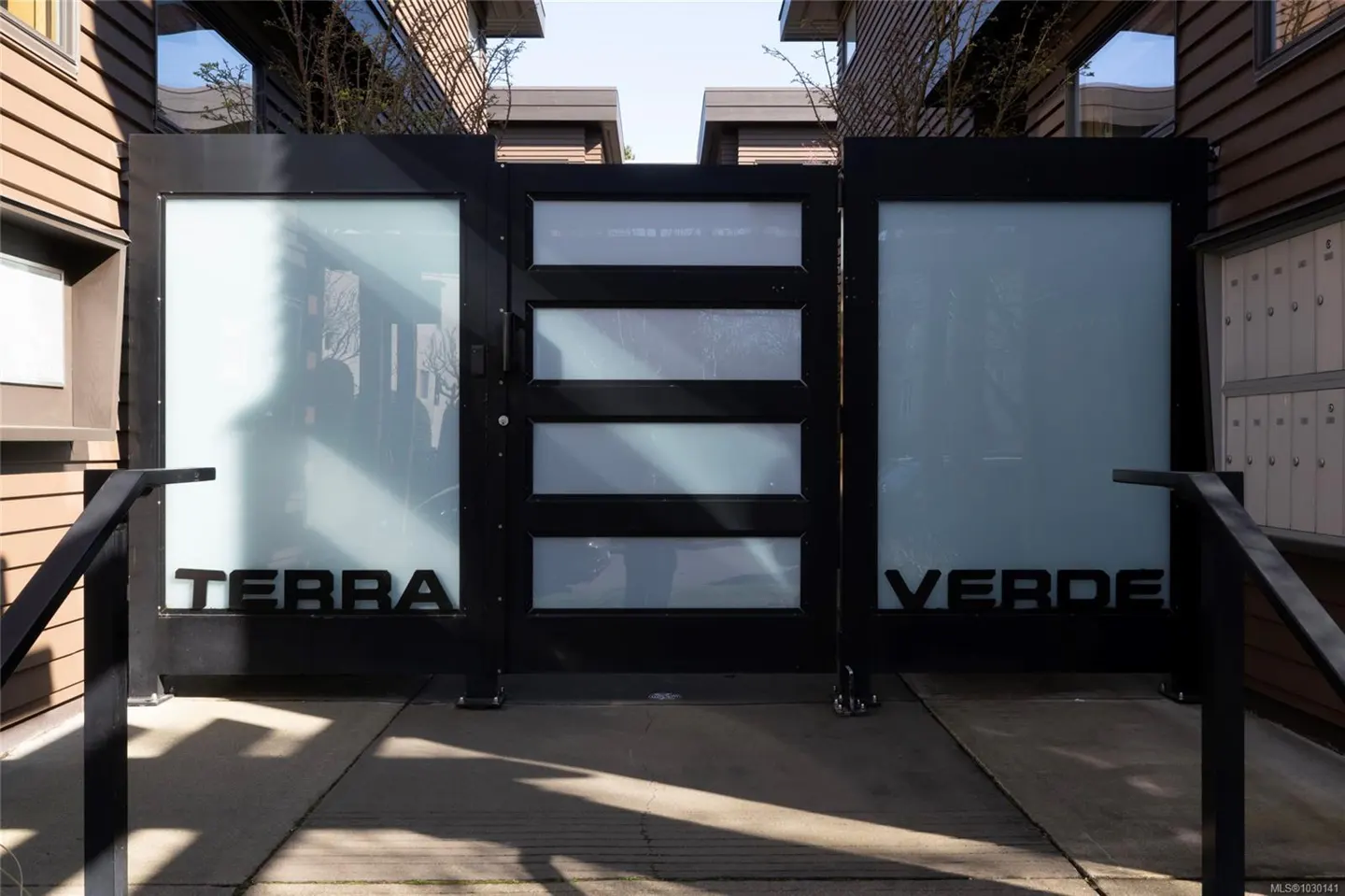 Exterior view of "Terra Verde" entrance gate with frosted glass panels and black metal frame, flanked by railings.