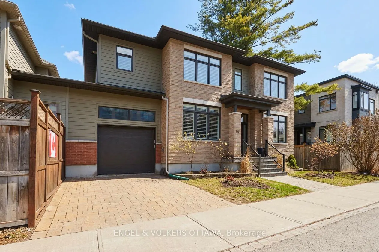 Two-story house with a stone and green siding exterior, black framed windows, and a dark garage door. A brick driveway leads to the garage.