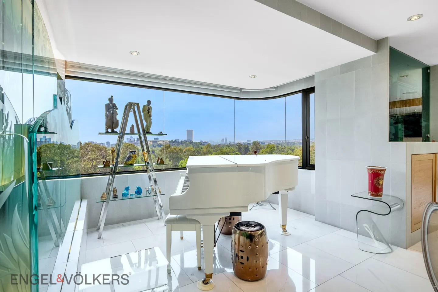 Bright room with a white grand piano, glass shelving, and a city view through a large window.