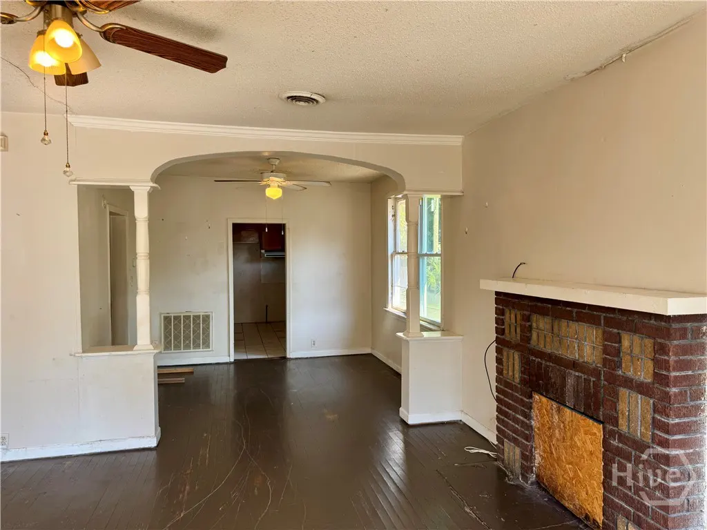 Living room with dark wood floors, a brick fireplace, arched entryway, and ceiling fans in a neutral-toned home.