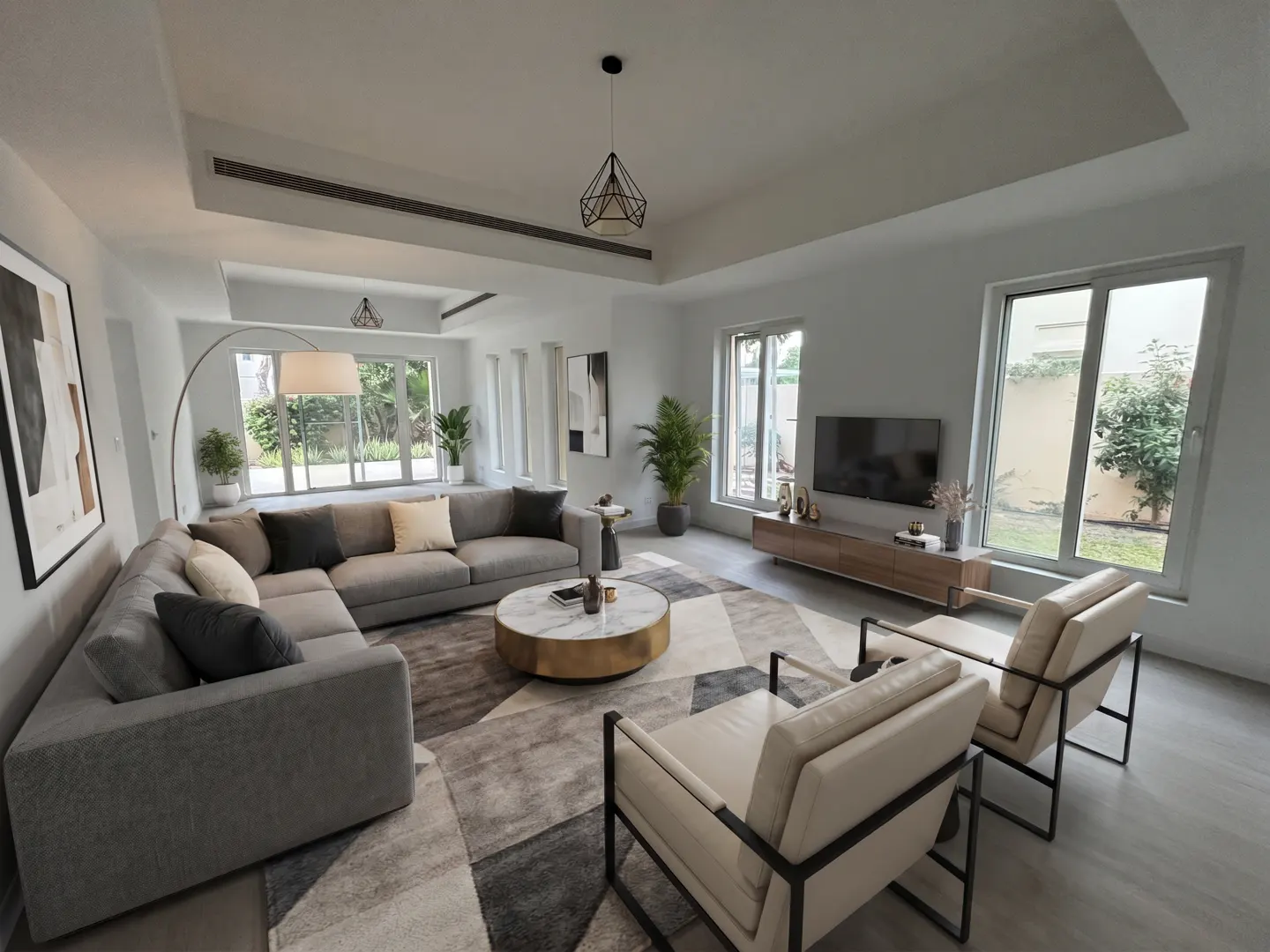 Bright living room with a gray sectional sofa, marble coffee table, and two cream-colored armchairs on a geometric rug. Large windows offer views of greenery.