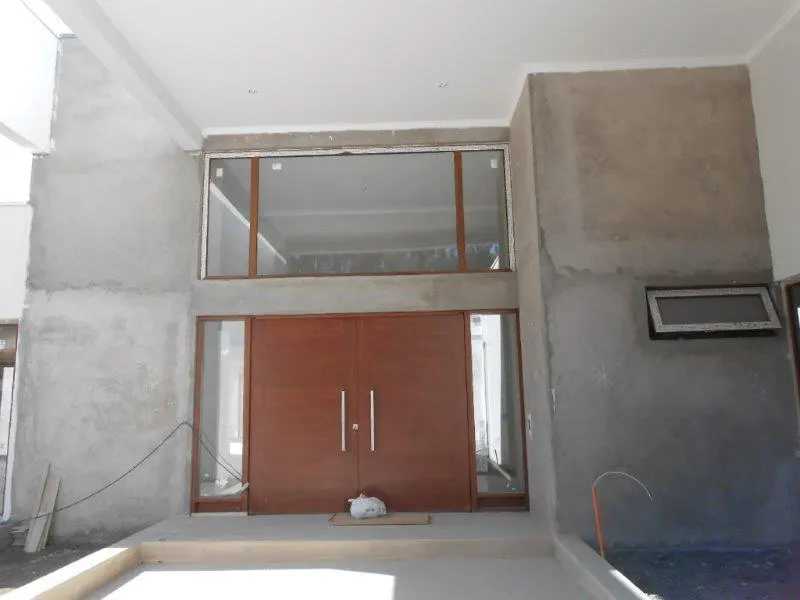 Exterior view of a modern home entrance with large brown double doors, a large window above, and gray concrete walls.