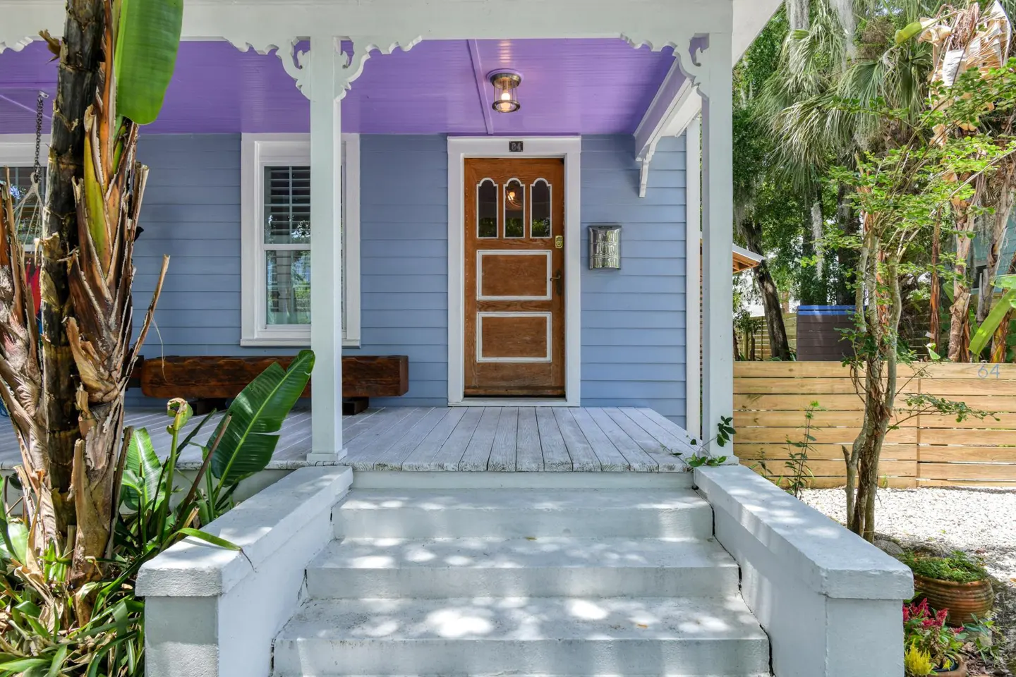 Front view of a light blue house with a purple porch ceiling, white trim, and a brown front door. Steps lead up to the porch.