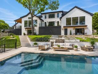 Modern white two-story house with a pool, patio furniture, and fire pit in the backyard on a sunny day.