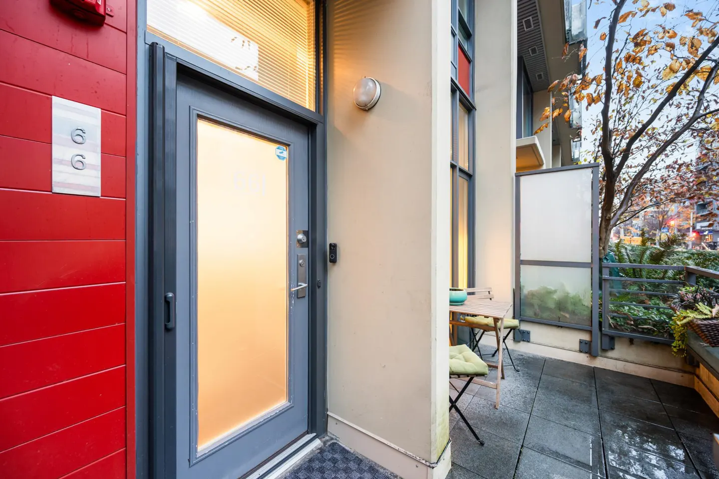 Exterior view of a condo with a red wall, a gray door, and a small patio with a table and chairs.