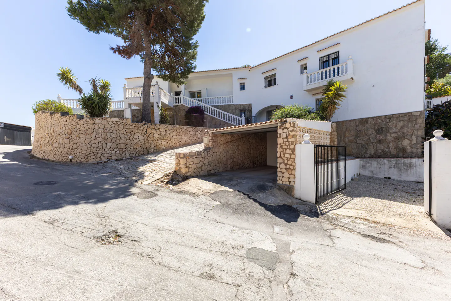 Exterior view of a white two-story house with a stone wall, carport, and black gate.
