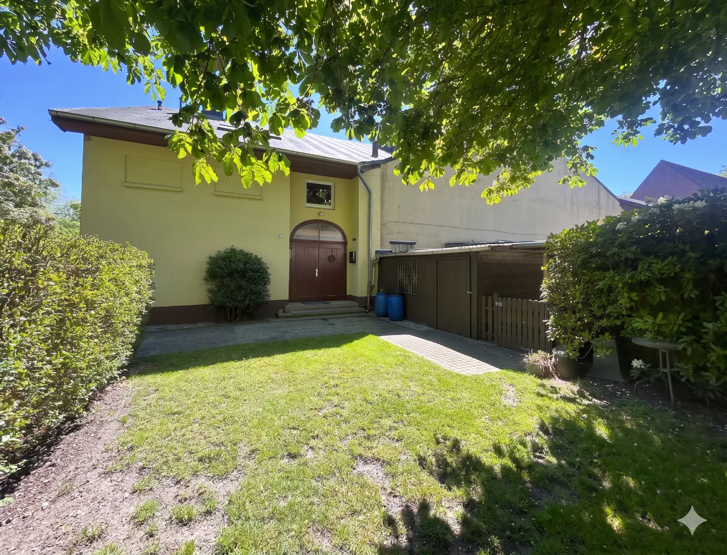 Exterior view of a two-story yellow building with a brown door, green lawn, and trees.