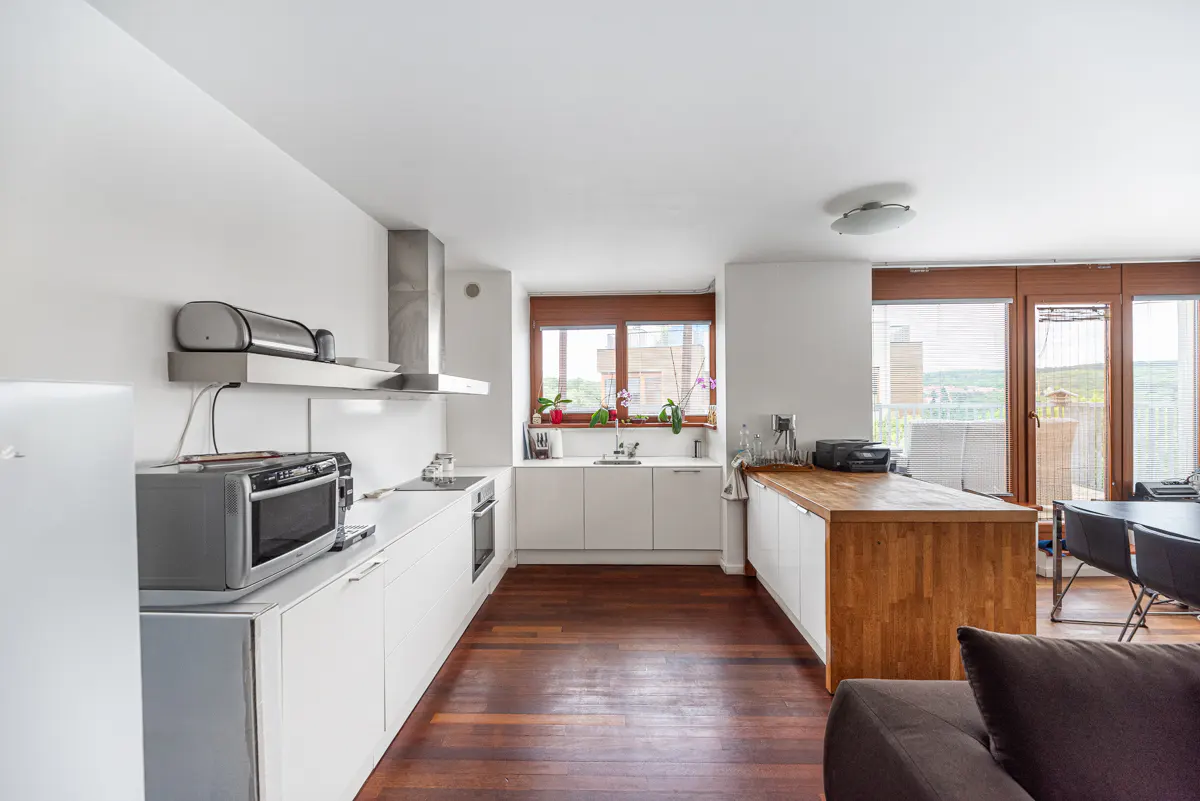 Bright, modern kitchen with white cabinets, stainless steel appliances, and a wood-topped island. Hardwood floors and large windows.