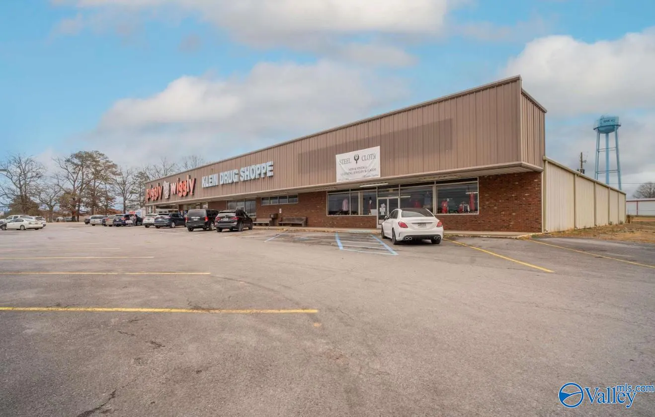 A long, one-story commercial building with a large parking lot and a blue water tower in the background.