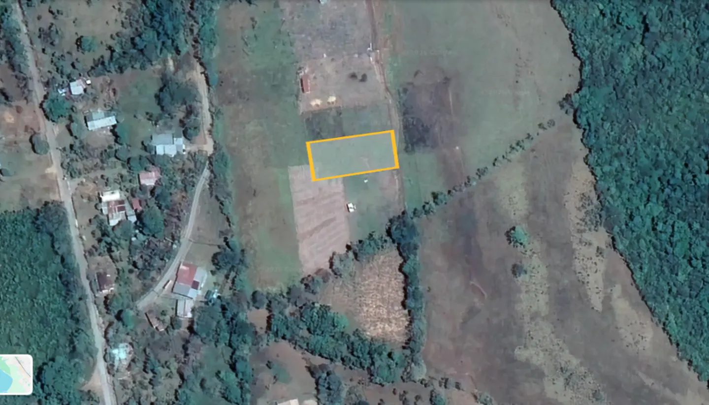 Aerial view of a rectangular plot of land outlined in yellow, surrounded by fields, trees, and a few houses.