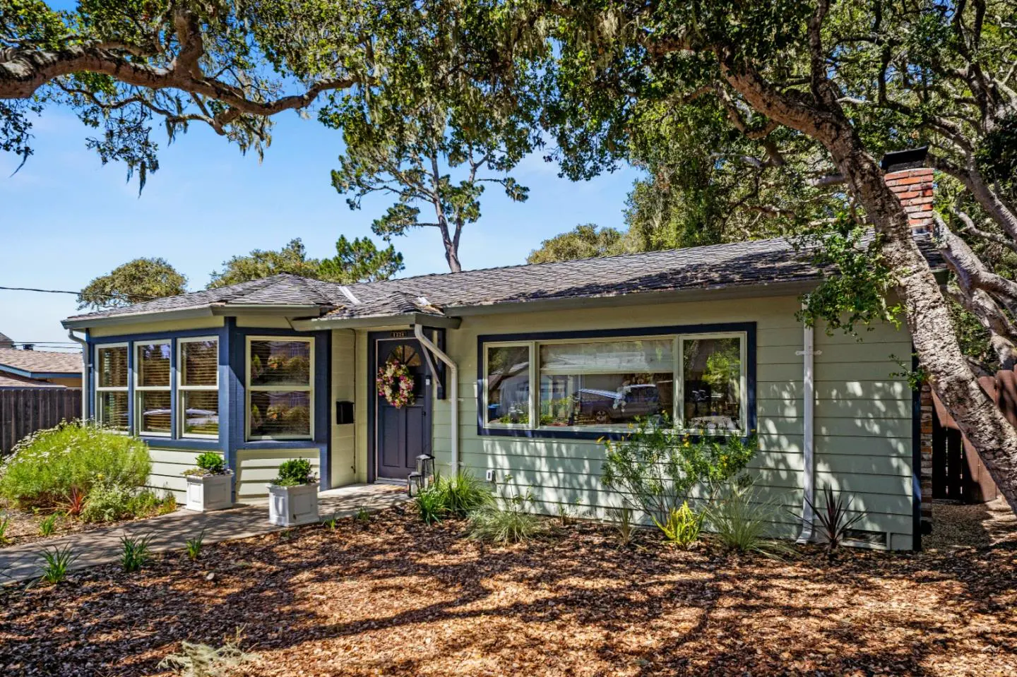 Exterior of a light green house with blue trim, a wreath on the front door, and trees.