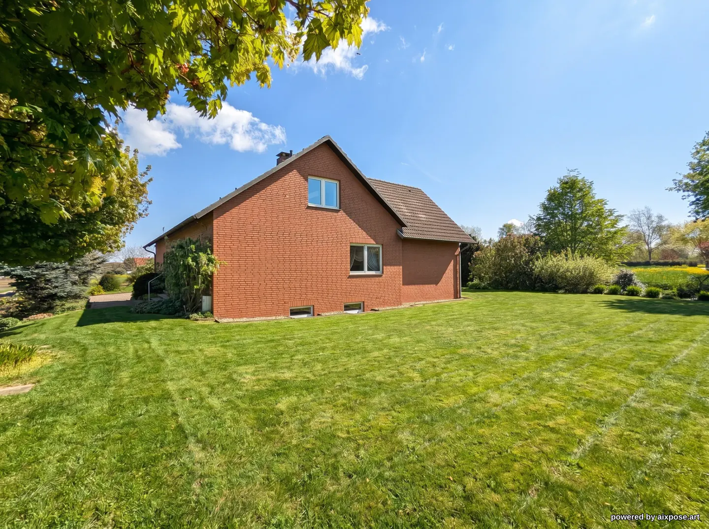 Brick house with a large green lawn under a blue sky with trees in the background.