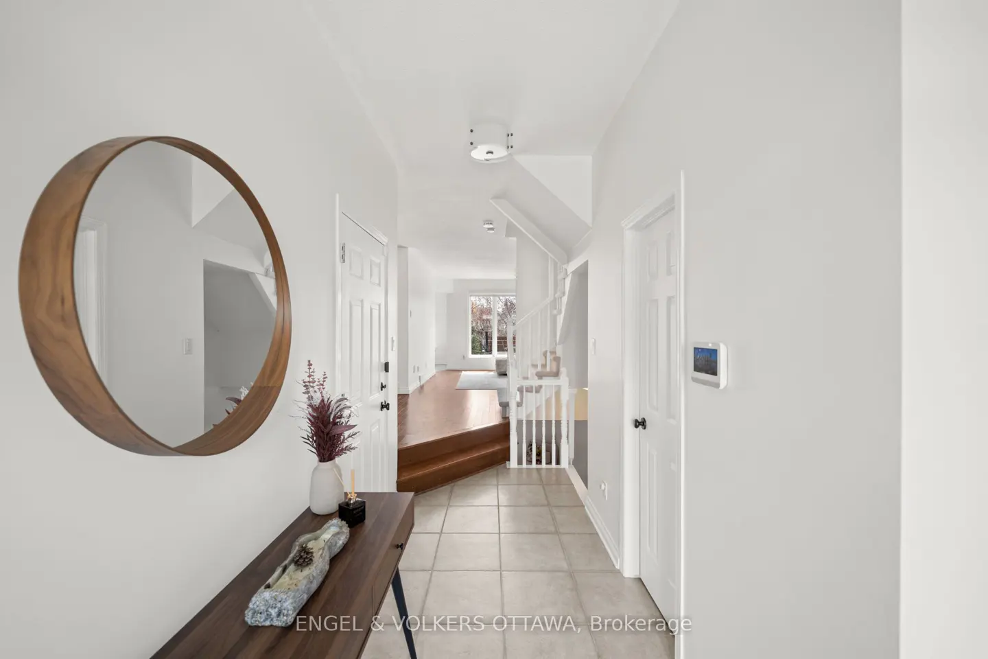 Bright foyer with a round wood-framed mirror, dark wood console table, and white walls leading to a staircase.