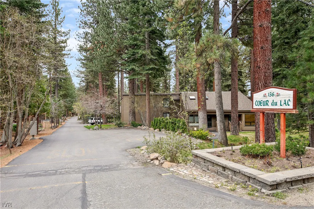 Exterior view of "Coeur du Lac" complex with a sign, trees, and a paved road leading to the building.