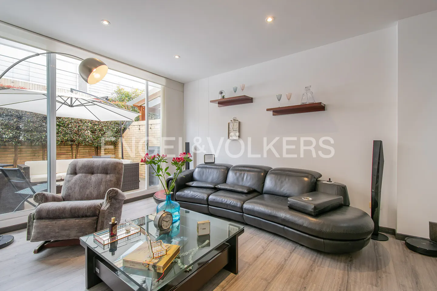 Living room with gray recliner, black leather sofa, glass coffee table, and outdoor patio view.